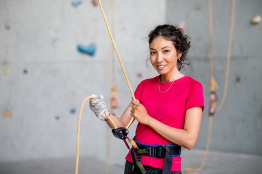 Portrait of beautiful woman rock climber belaying another climber with rope. Indoors artificial climbing wall and equipment. clipart