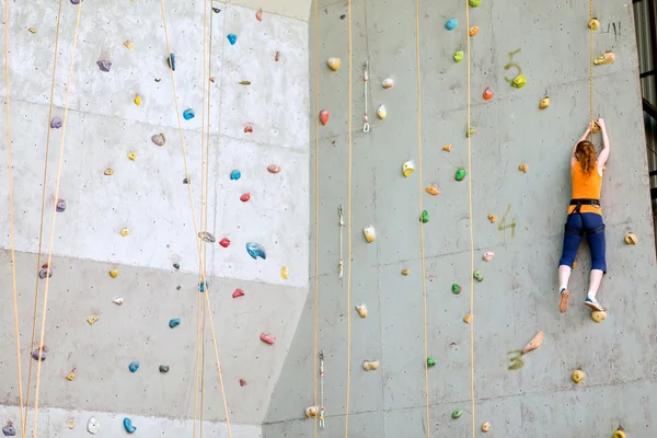Schöne junge Frau beginnt, große künstliche Wand zu erklimmen — Stockfoto