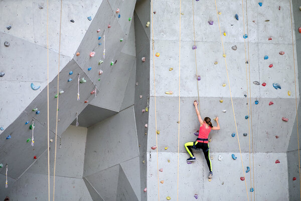 Beautiful young woman starts to climbing big artificial wall