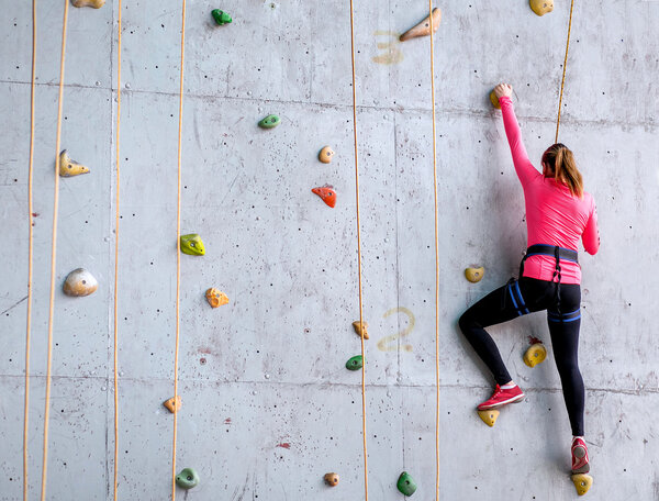 Beautiful young woman starts to climbing big artificial wall