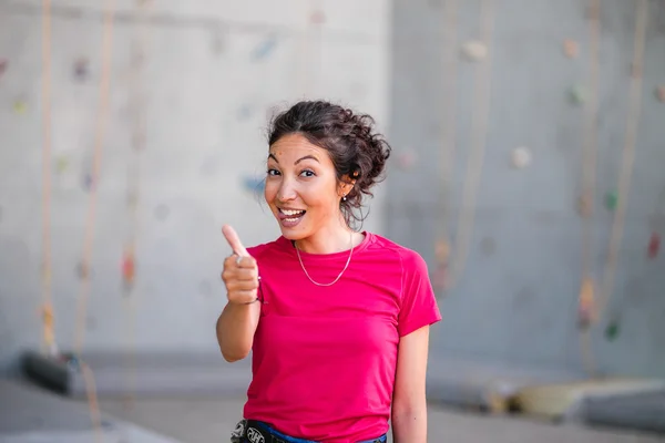 Glada leende vacker ung kvinna visar tummen upp gest, klättring vägg bakgrund — Stockfoto