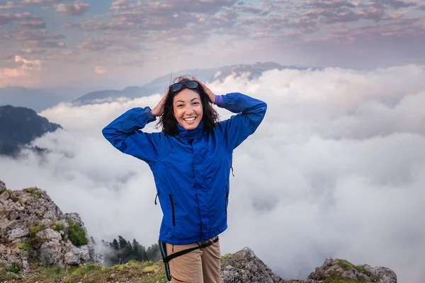 Mujer joven mochilero senderismo en la cima de la montaña por encima de las nubes y la niebla — Foto de Stock