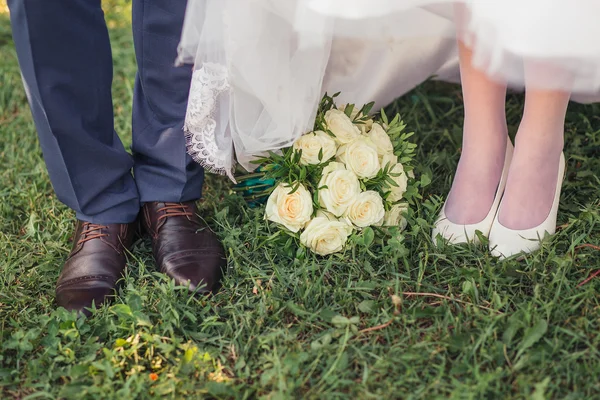 Pés e sapatos recém-casados na grama no jardim e bouqu nupcial — Fotografia de Stock