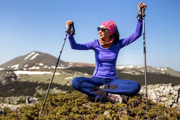 Mujer sosteniendo bastones de senderismo sentado en la pared contra la montaña — Foto de Stock