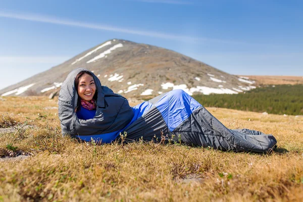 A turisztikai nő természetjáró egy hálózsákban a füvön, a hegy — Stock Fotó