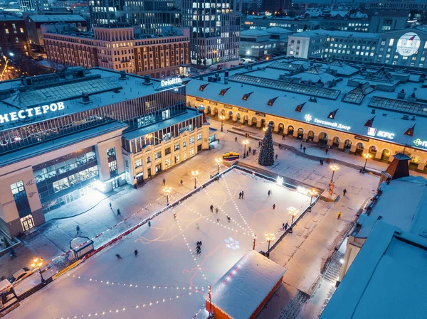 23 Aralık 2020, Ufa, Rusya: Alışveriş merkezinin yakınlarındaki muhteşem bir kış şehrindeki bir Noel ağacının arka planındaki buz pateni pistinde eğlenen ve kayan insanların hava manzarası