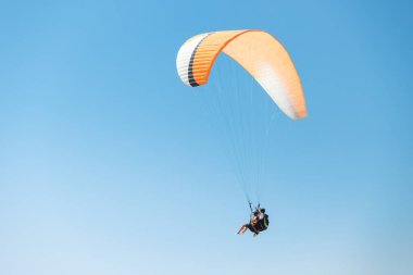 Eğitmen ve öğrenci büyük bir paraglider üzerinde havada uçuyor. Arka planda mavi gökyüzü. Aktif yaşam tarzı ve adrenalin bağımlılığı