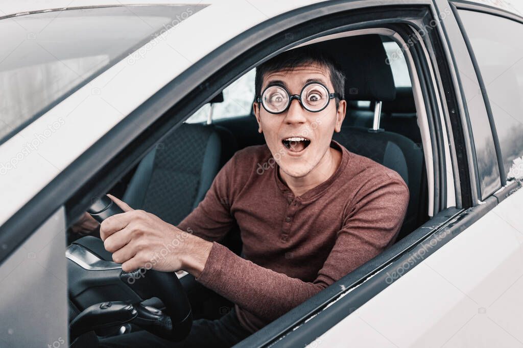 ridiculous geek driver is staring at the camera and holding the steering wheel. Concept of a novice driver and learning to drive in the city