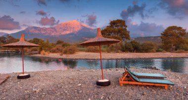 Güneş yataklı, güneşli, güneşli ve arka planda Tahtali Dağı olan pembe gölgeli bir gün batımı. Türkiye 'de Tekirova ve Kemer tatil beldesinde turizm ve dinlenme