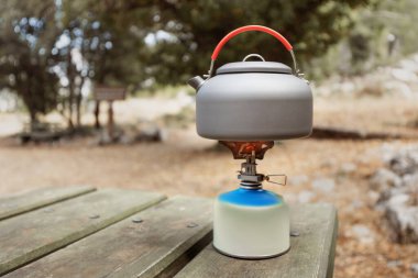 Bir kamp alanındaki gaz ocağında çaydanlıkta sıcak çay ya da kahve pişirmek. Yürüyüş için sofra takımı ve ekipman kavramı