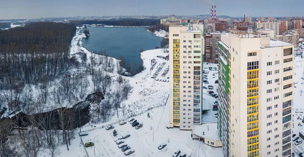 Multi-storey residential high-rise buildings form a neighboring residential area near a picturesque lake in the city. Drone Aerial view in winter