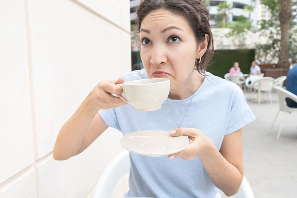 Woman takes a sip of coffee and makes a disgusting grimace. The concept of bad smell or trouble waking up and insomnia