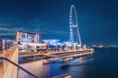 Mavi Sular Adası 'ndaki yaya köprüsünden gece görüşü dekoratif ışıklandırması ve dünyanın en büyük dönme dolaplarından biri olan Dubai Göz.