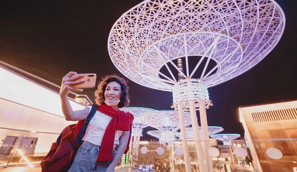 Woman tourist taking selfie photo at famous Dubai tourist Attraction - Neon futuristic glowing metal super trees on bluewaters Island.