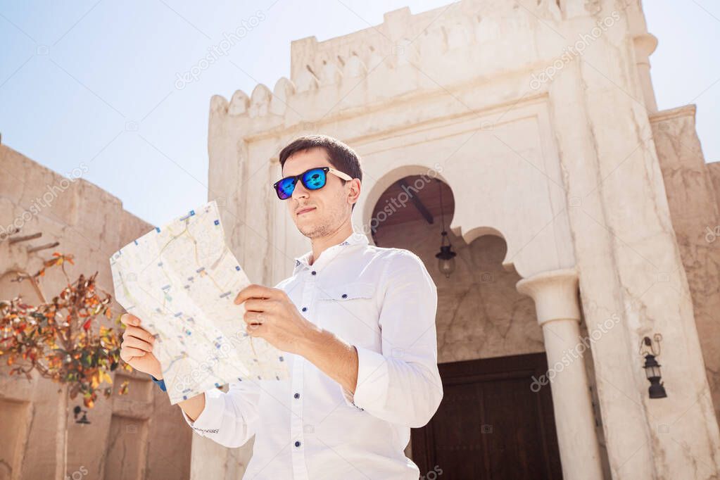 Handsome man in white shirt looking at map and looking for ways to discover new attractions in the famous old Bur Dubai Creek area. Concept of navigation and tourist spots