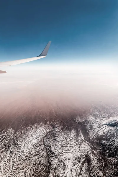 Vista Janela Avião Com Uma Asa Terreno Dobrado Coberto Neve — Fotografia de Stock