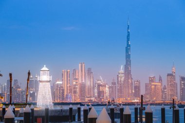 Illuminated decorative lighthouse at the background of famous Burj Khalifa skyscraper tower in the Dubai Creek Marina Harbor. Travel and tourist destinations