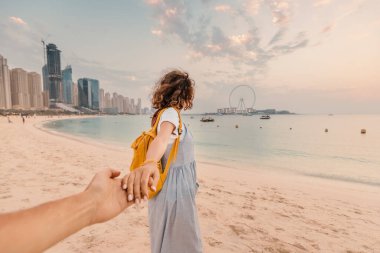 Beni takip ettiren mutlu kadın turist Dubai 'nin JBR bölgesinde kumlu bir plajda poz veriyor ve Dönme Göz' ün panoramik manzarasına hayran.