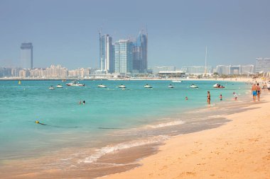 25 Şubat 2021, Dubai, BAE: Kumlu sahil boyunca Palm Jumeirah adası manzaralı bir grup turist yürüyor. Tatilciler yüzer ve iyi vakit geçirirler.