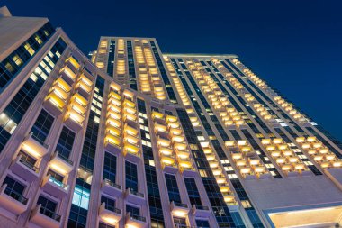 Geceleyin Dubai tatil köyündeki modern bir otel binasının ön cephesinde birçok balkon deseni aydınlandı.