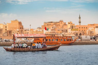 23 Şubat 2021, Dubai, BAE: Abra Dhow ahşap botlar Dubai Deresi 'nin bir kıyısından diğer kıyısına ve arka planında cami minaresi olan yolcuları taşır.