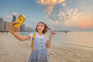 Kadın seyahat blogcusu sosyal ağları için gökdelenlerin ve Dubai 'deki ünlü Ain Ferris Wheel' in arkaplanına karşı selfie çekiyor.