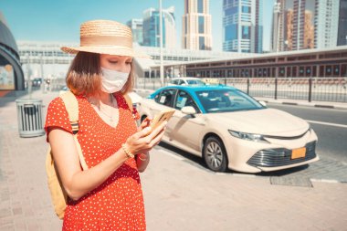 Covid salgını sırasında koruyucu maskeli bir kadın turist şehirde bir gezi için akıllı telefondan taksi çağırmış.
