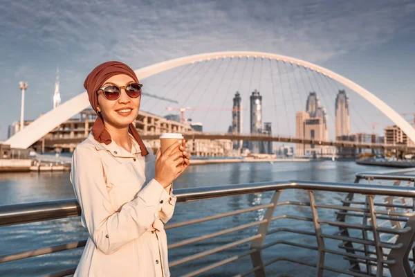Szczęśliwa Muzułmanka Żółtym Plecakiem Spaceruje Wzdłuż Nabrzeża Dubai Canal Pije — Zdjęcie stockowe