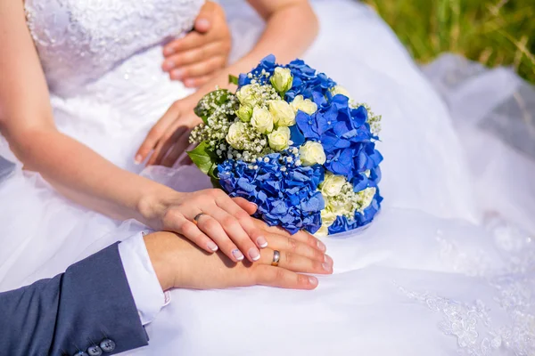 Mãos de noivo e noiva em um buquê de casamento — Fotografia de Stock