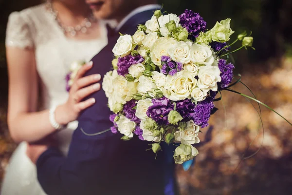 Bride hugs groom with wedding bouquet — Stock Photo, Image