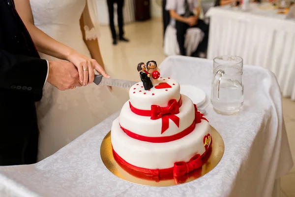Casal corte bolo de casamento com fitas vermelhas e a estatueta — Fotografia de Stock