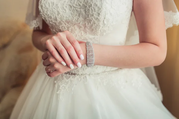 As mãos doces com a pulseira da noiva no vestido branco de cadarço — Fotografia de Stock