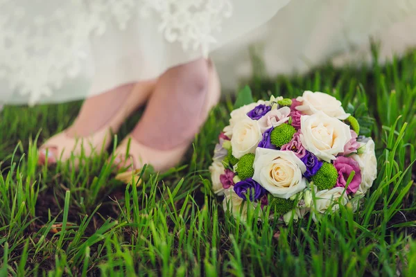 El ramo nupcial con las piernas de la novia sobre la hierba verde brillante — Foto de Stock