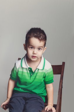 Şirin çocuk beyaz arka plan üzerinde bir tahta sandalyede oturan