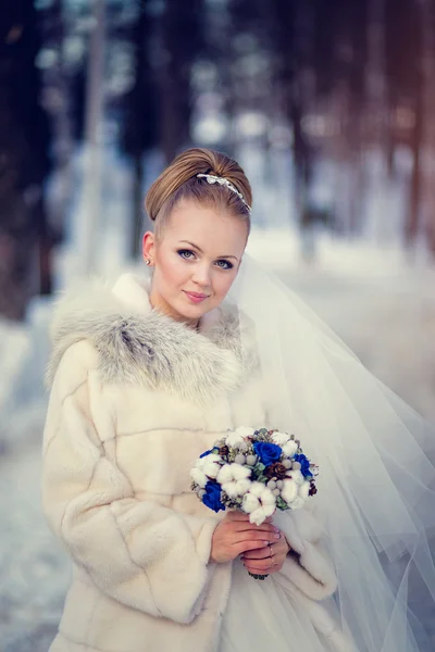 La novia en el abrigo de piel con el ramo y el velo en la nieve invernal — Foto de Stock