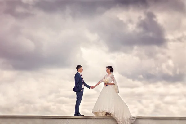Bride and groom standing on the background of stormy sky with cl — Stock Photo, Image