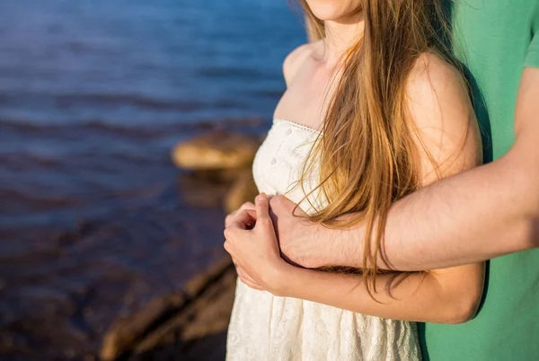 Pareja irreconocible en el amor abrazándose en la orilla del mar. las manos son —  Fotos de Stock