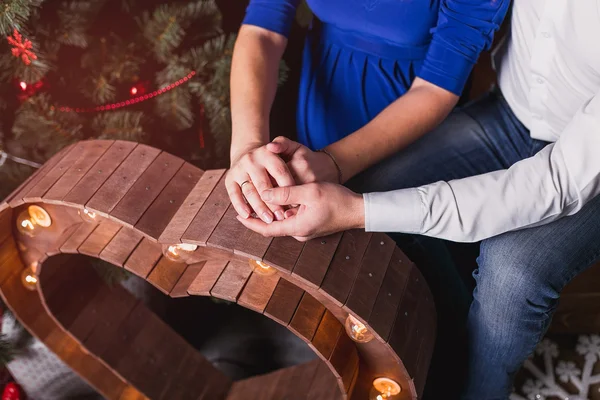 Ungt par håller händerna framför en julgran — Stockfoto