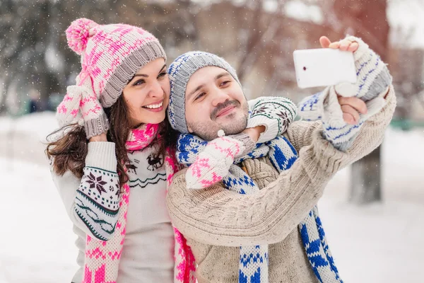 Casal apaixonado fazendo selfie no inverno ao ar livre em suéteres, cachecol e mitenes — Fotografia de Stock