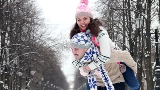 Par njuter av deras vinter helg tillsammans, killen som innehar hans flickvän piggyback — Stockvideo