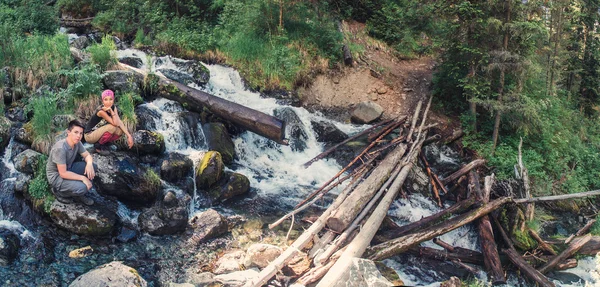 Dos turistas sentados cerca del destruido puente de troncos en bruto — Foto de Stock