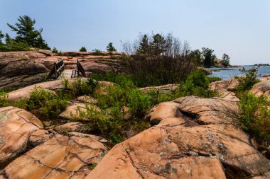 Gürcistan Körfezi kıyısındaki engebeli granit kayaların üzerinde tahta bir yaya köprüsü. Killarney İl Parkı, Ontario, Kanada