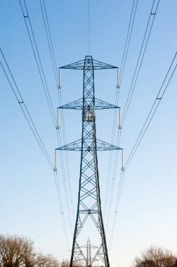 Sabahın erken saatlerinde mavi gökyüzüne karşı yüksek voltajlı elektrik hatları.