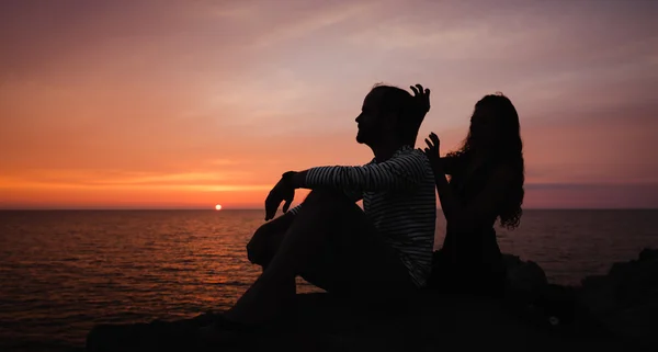 Jong koppel in liefde tegen zonsondergang op zee — Stockfoto