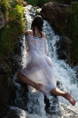 Beyaz elbiseli genç kadın şelalenin serinliğinin ve tazeliğinin tadını çıkarıyor.