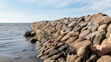 Genç, çıplak bir kadın taştan bir dalganın üzerinde poz veriyor. Çıplak esmer doğanın tadını çıkarıyor.