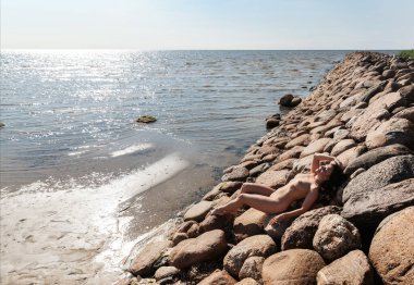 Genç, çıplak bir kadın taştan bir dalganın üzerinde poz veriyor. Çıplak esmer doğanın tadını çıkarıyor.