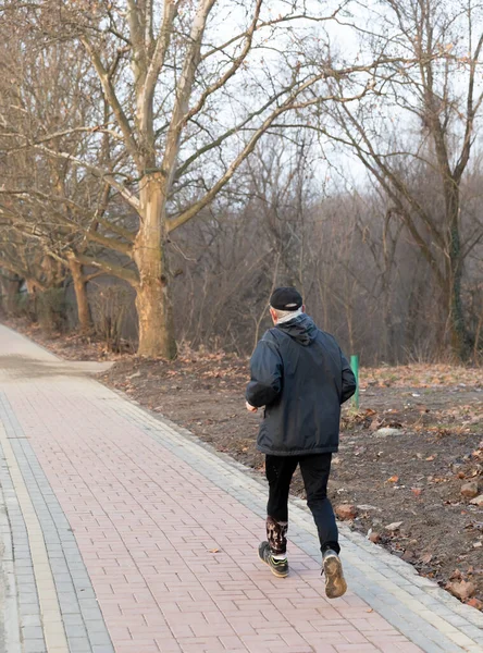 Healthy and active lifestyle concept. An elderly sporty man runs along the park alley during morning workout.