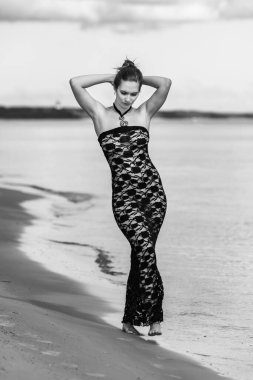 Siyah dantel elbiseli genç, kızıl saçlı kadın sahilde çıplak poz veriyor.