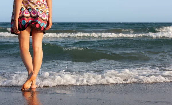 夏のドレスを着た若い美しい女性が砂浜の海の水の中に立って波と潮風を楽しんでいます — ストック写真